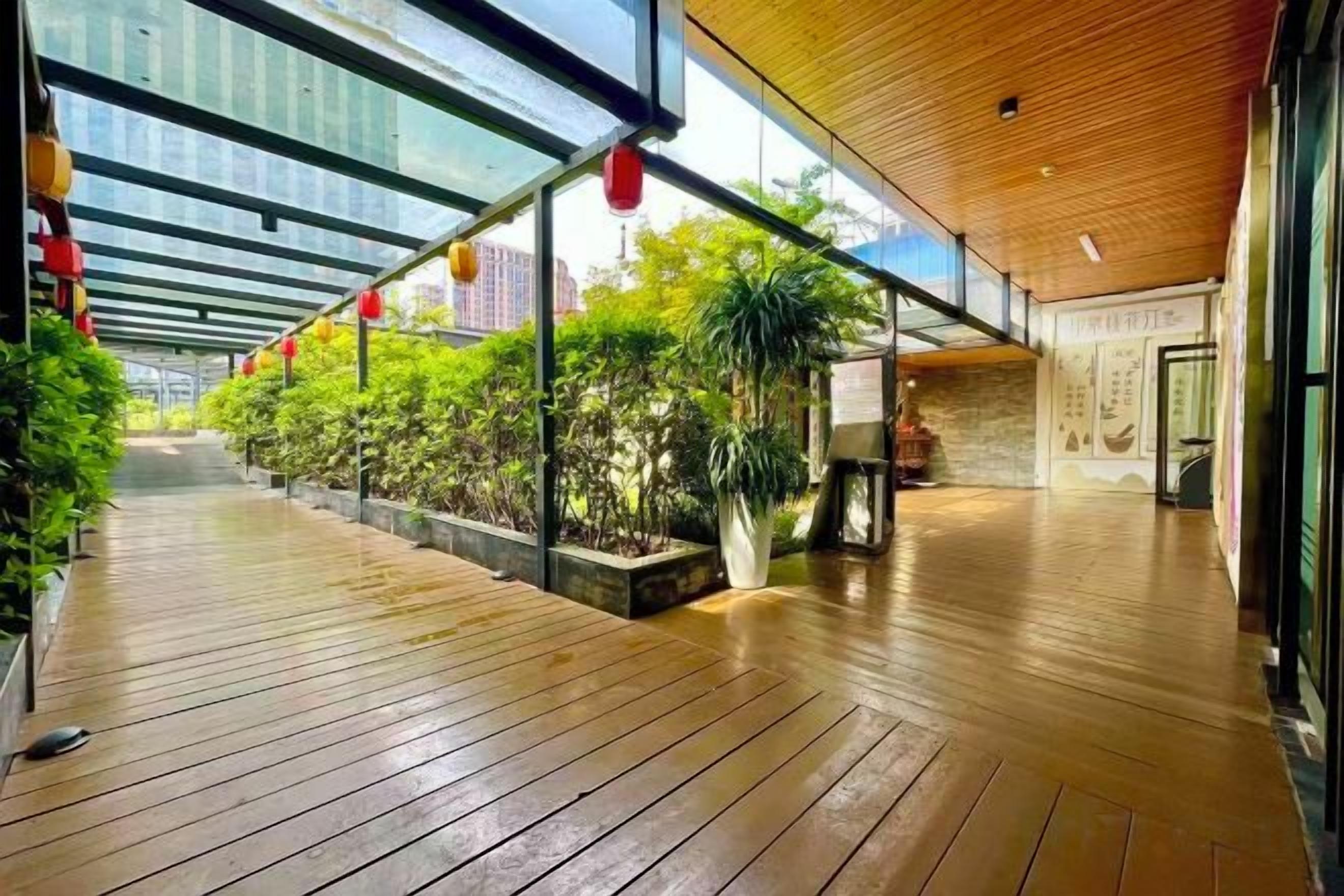 Un paseo techado con piso de madera, macetas con plantas y faroles rojos.