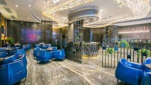 Un moderno vestíbulo de hotel con asientos azules, suelo de mármol y un diseño de lámpara de techo único.