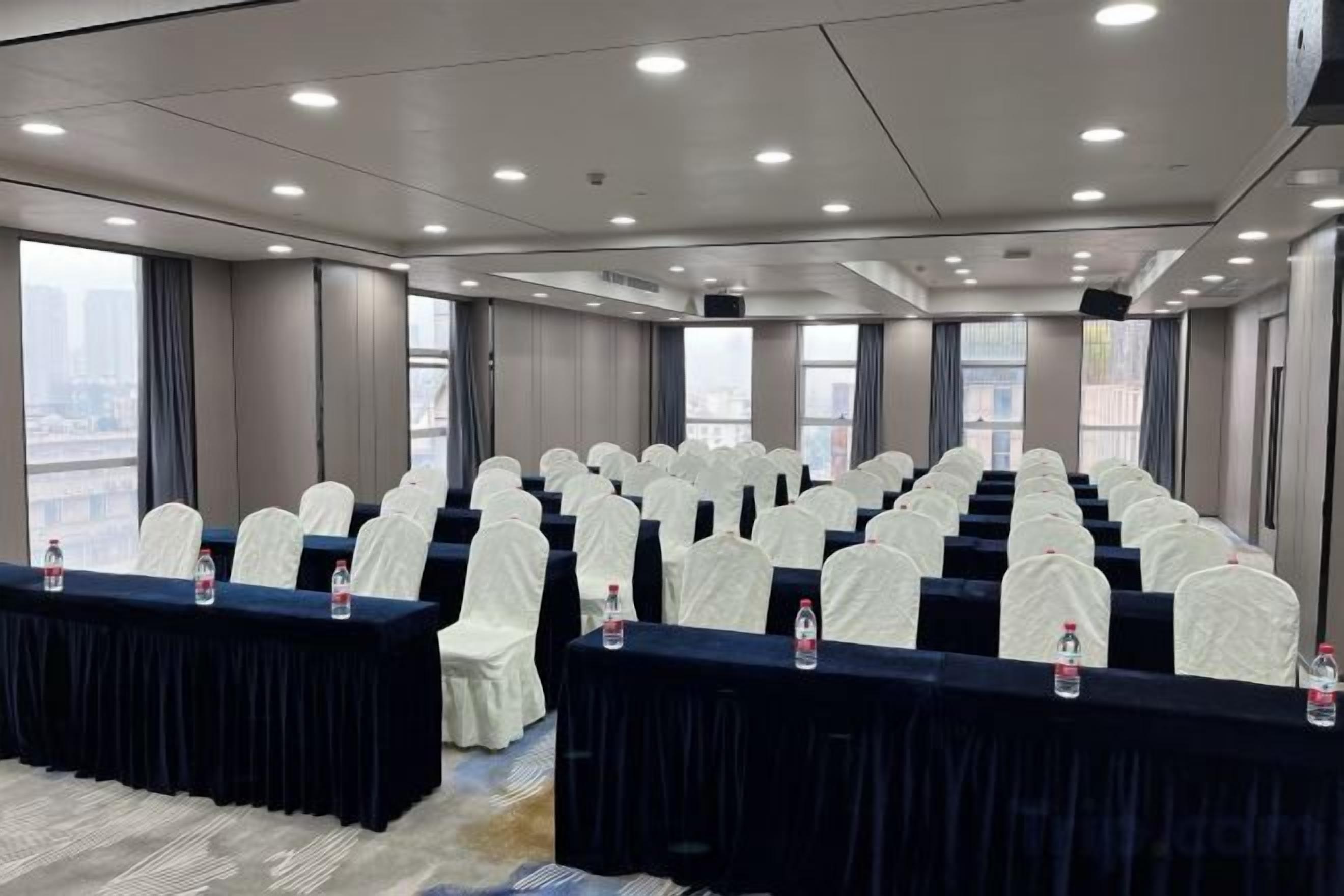 A conference room with rows of chairs, tables with water bottles, and large windows offering a city view.