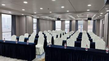 A conference room with rows of chairs, tables with water bottles, and large windows offering a city view.