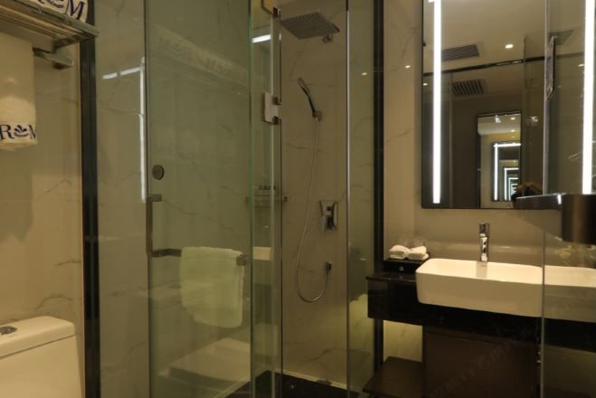 Un baño moderno con ducha acristalada, lavamanos blanco y un espejo grande.