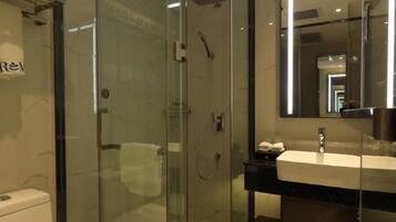 Un baño moderno con ducha acristalada, lavamanos blanco y un espejo grande.