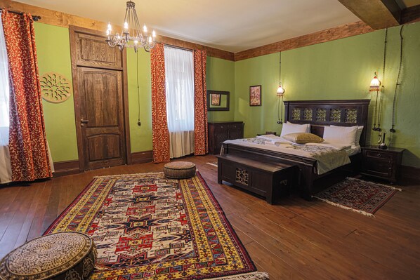 Un dormitorio tradicional con suelo de madera, una cama grande con cabecera, una mesita de noche, un banco y una araña.
