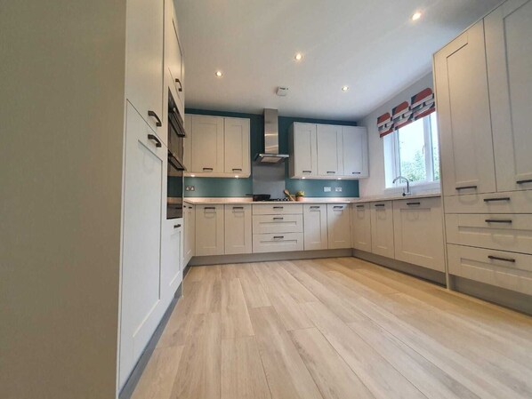 Kitchen features a central island with a sink and stove, surrounded by white cabinets with black handles.
