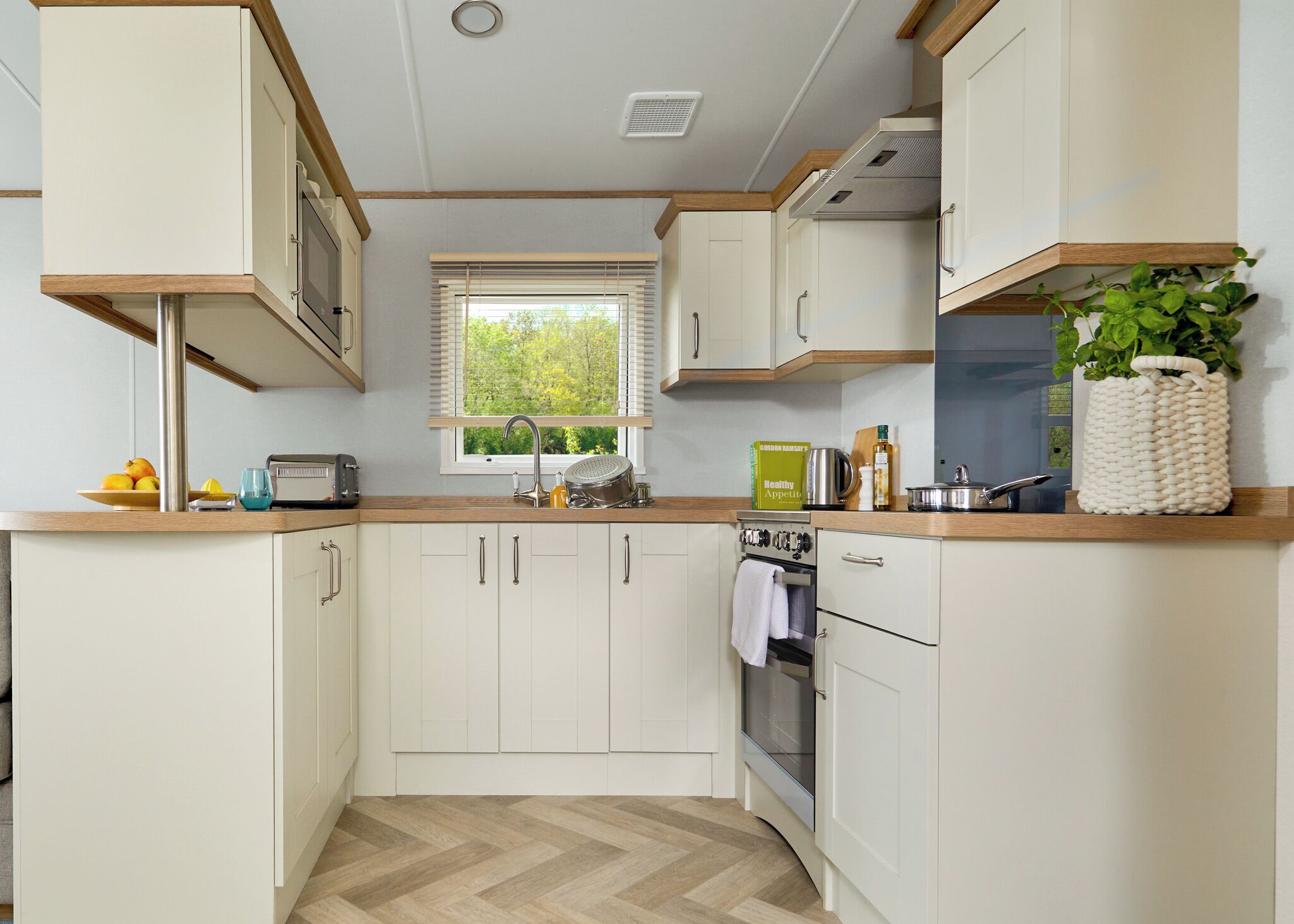 A modern kitchen with white cabinets, a wooden countertop, a window with blinds, and a potted plant.