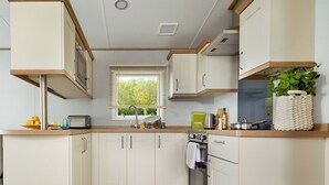 Una cocina moderna con armarios blancos, encimera de madera, ventana con persianas y una planta en maceta.