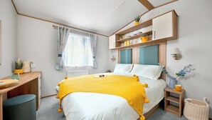 Un dormitorio con cama, mesita de noche, lámpara y ventana con cortinas.