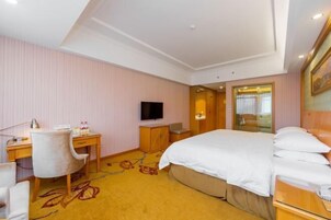 Habitación de hotel con cama, escritorio, silla, televisor y piso alfombrado.