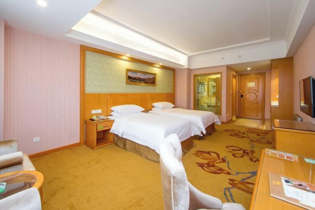 A hotel room with two beds, a desk, a chair, and a television.