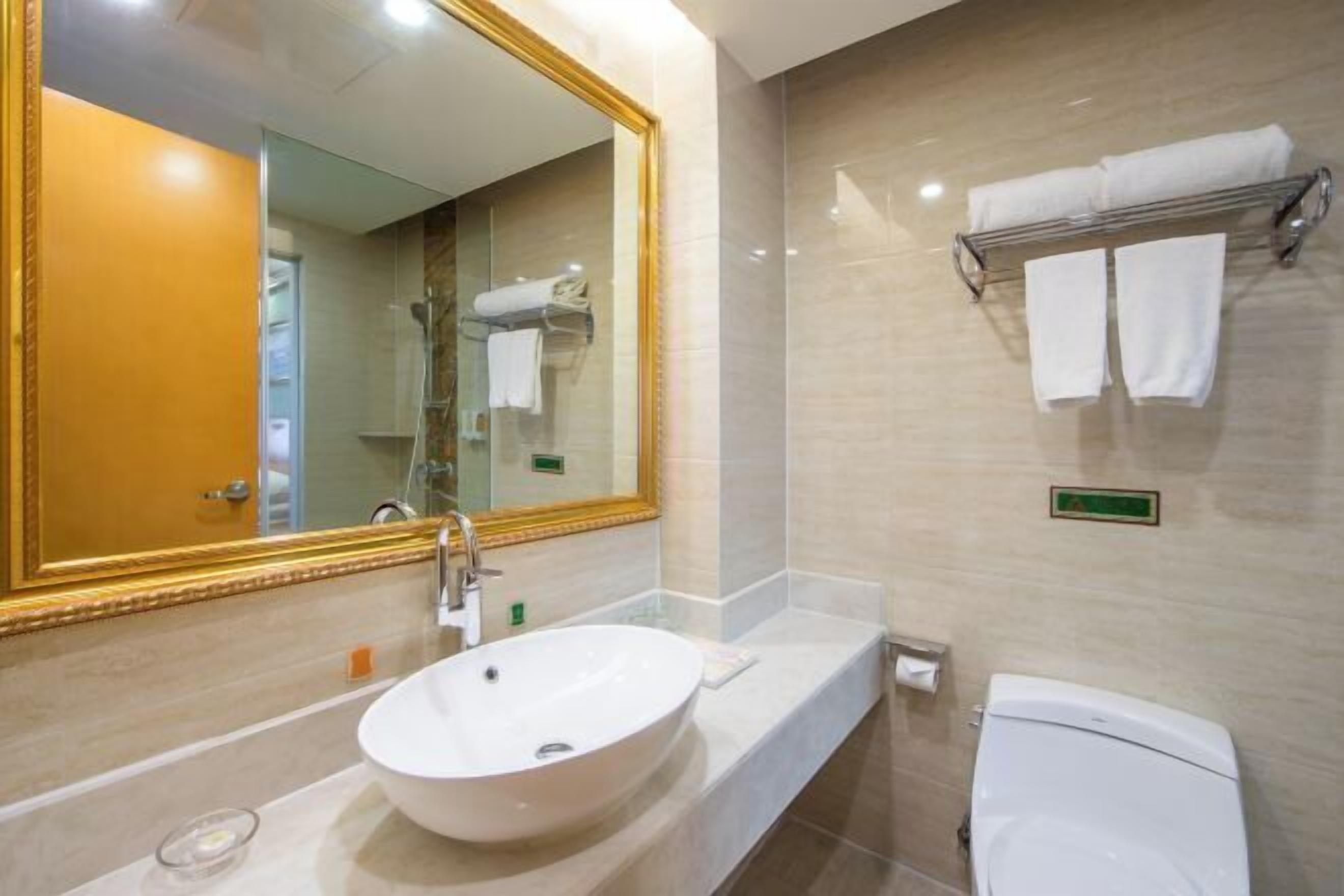 A bathroom with a large mirror, a sink, a toilet, and a towel rack.
