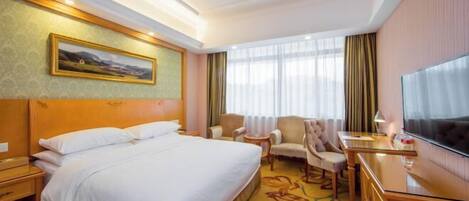 A hotel room with a bed, a desk, a chair, a TV, and a painting on the wall.