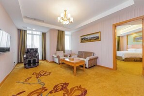 A hotel room with a massage chair, a sofa, a coffee table, a bed, and a painting on the wall.