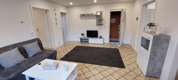 A living room with a sofa, a coffee table, a TV, and a fireplace. There are doors leading to other rooms. - Ferienwohnung im Schönen Odenwald (Mörlenbach)