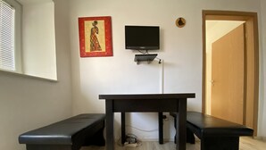 A room with a wooden floor, a black table with two benches, a television mounted on the wall, and a door. - Apartment 2,5 rooms in 2nd stock with roof teracce (Vodice)