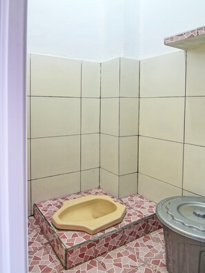 Une petite salle de bain carrelée, avec des toilettes à la turque et une poubelle.