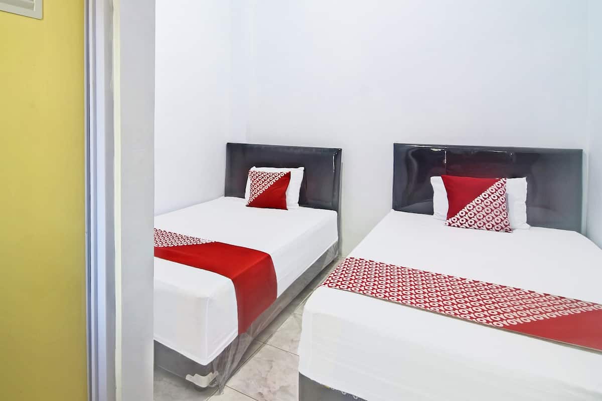 Two single beds with black headboards and red and white patterned bedspreads in a room with white walls and a yellow door.