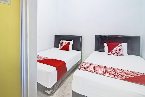 Deux lits simples avec des têtes de lit noires et des couvre-lits à motifs rouges et blancs, dans une pièce aux murs blancs et à la porte jaune.