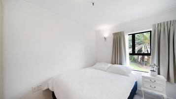 Een slaapkamer met een bed, nachtkastje, raam met gordijnen en uitzicht op het landschap.