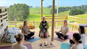 A group of people meditating on a wooden deck with a view of green fields.