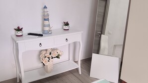 A room with a white console table, a flat-screen TV mounted on the wall, a mirror, and a small potted plant. - Renovated two-bedroom apartment, parking space, by the sea. (Marina di Caronia)
