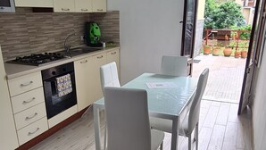 A compact kitchen with a gas stove, oven, and a dining area with a table and chairs. - Renovated two-bedroom apartment, parking space, by the sea. (Marina di Caronia)