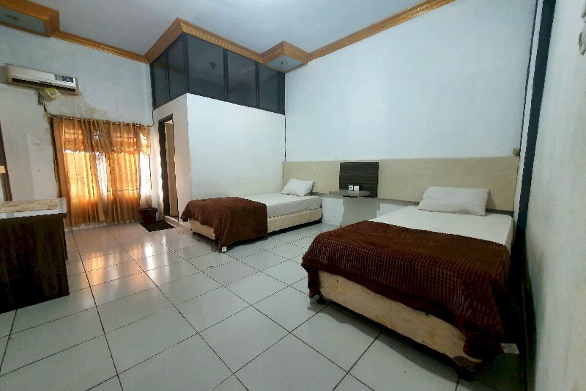 A hotel room with two beds, a small desk, and an air conditioning unit.