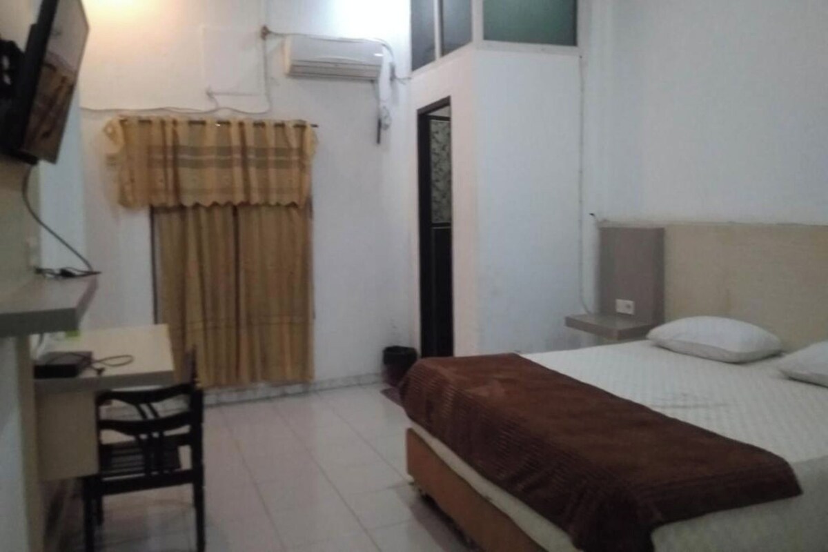 A bedroom with a bed, a desk, a chair, and a window with curtains.
