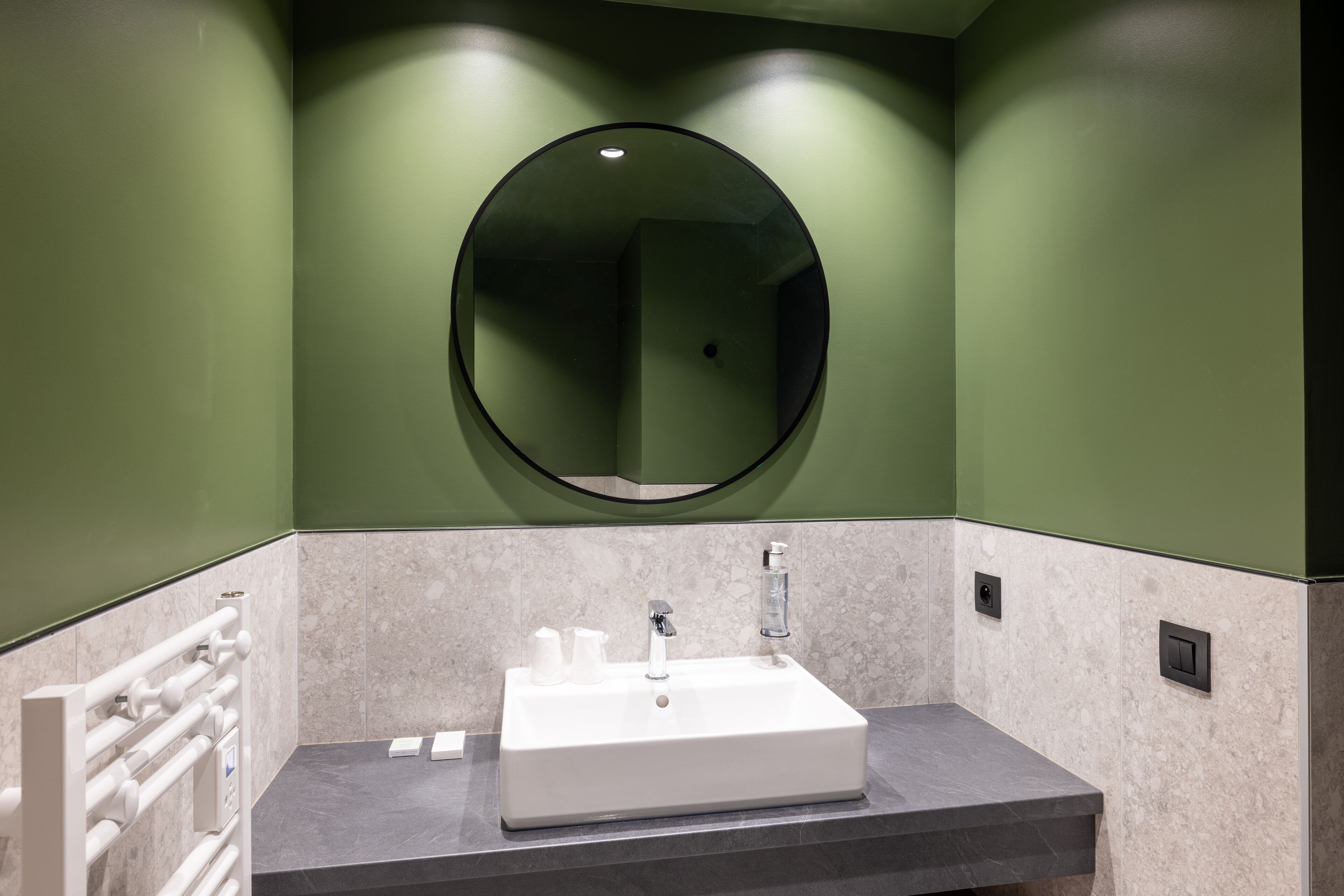 Un baño con un lavamanos blanco, un espejo y paredes verdes.