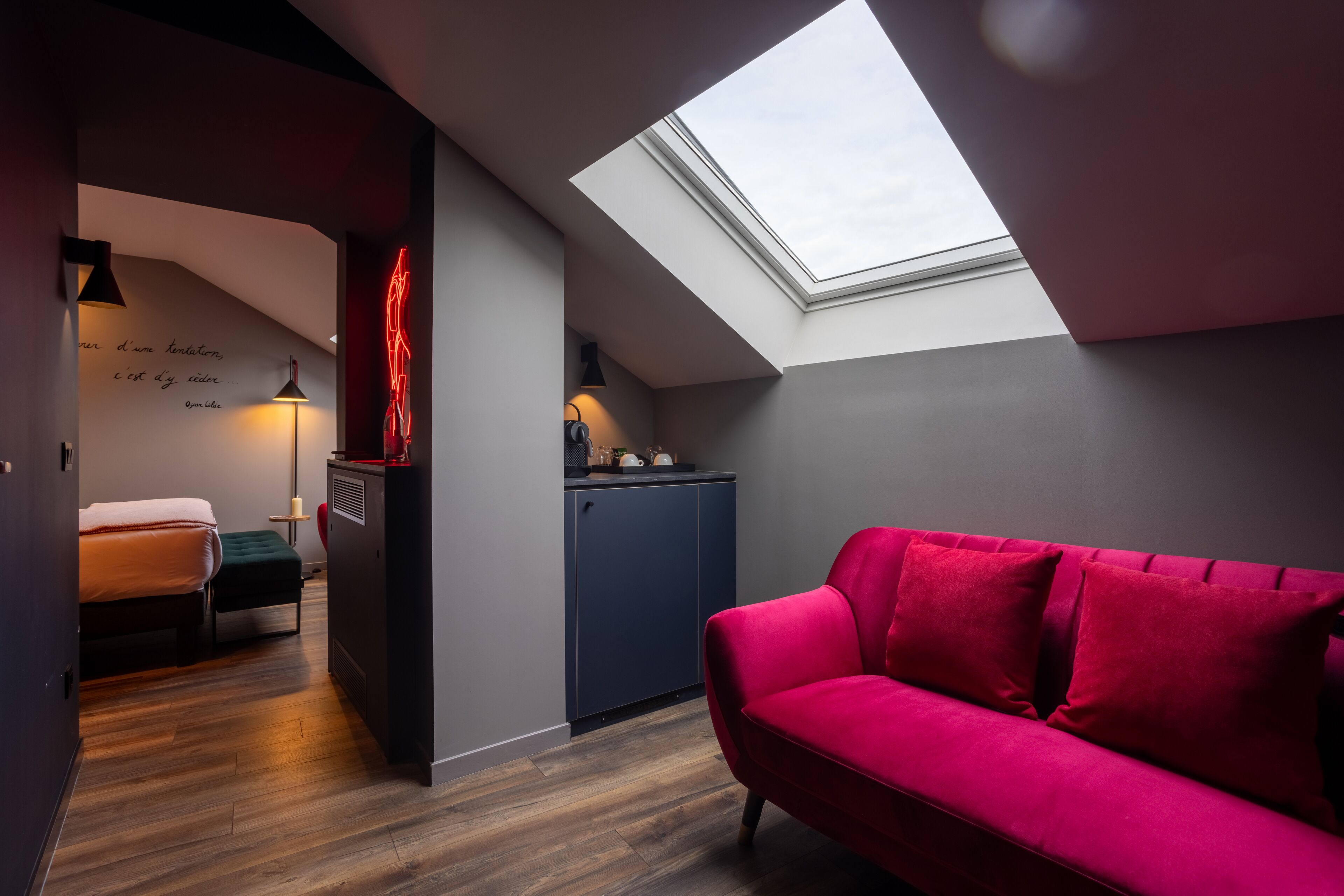 A compact room with a skylight, a red sofa, a bed, and a kitchenette.