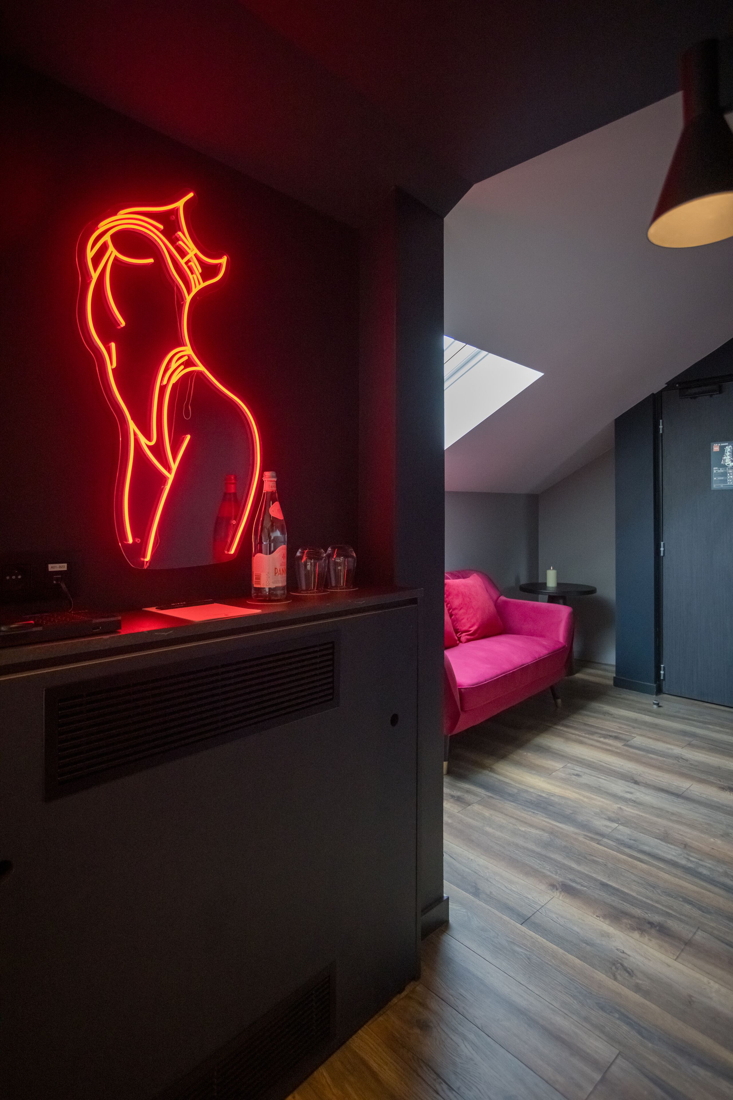 A modern room with a neon art installation, a sofa, a small table, and a skylight.