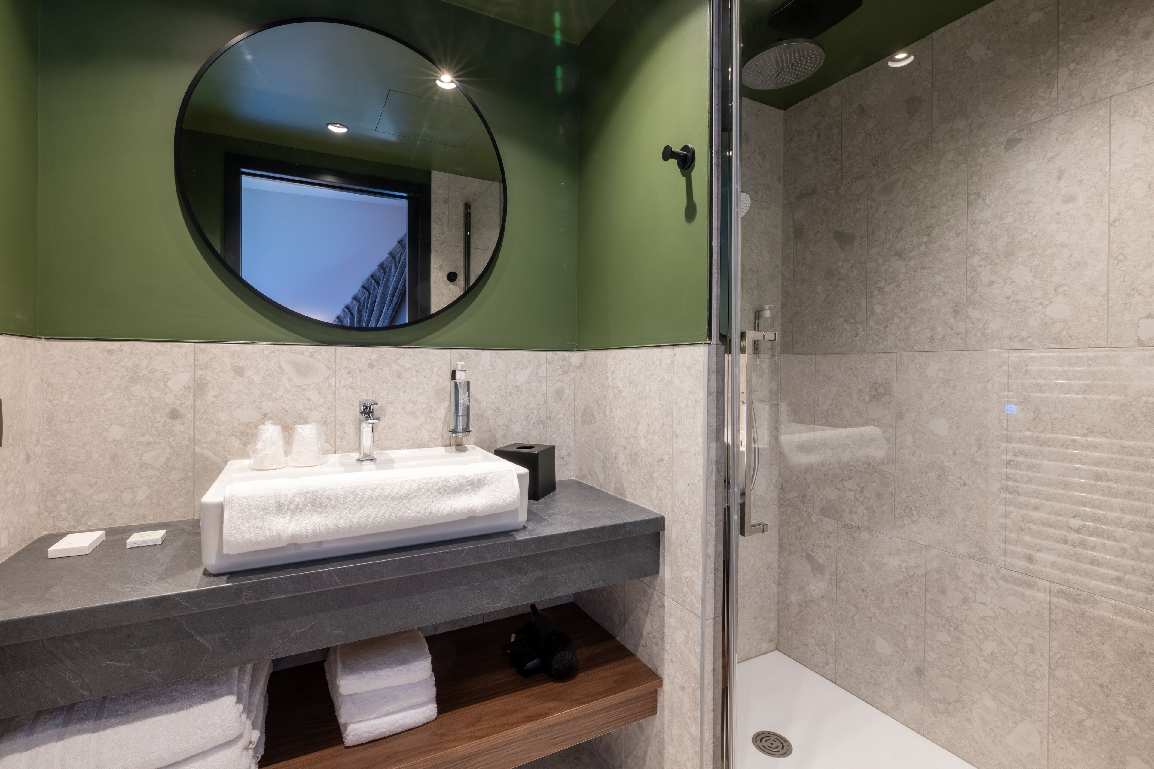 Un baño moderno con un espejo redondo, un lavabo con una toalla y una zona de ducha.