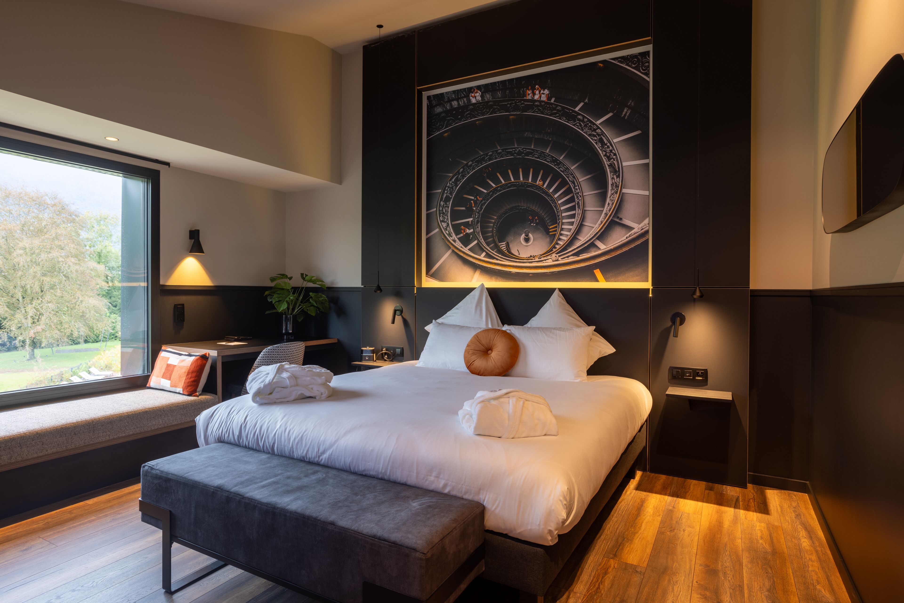 Une chambre d’hôtel moderne avec un grand lit, une banquette, un bureau et une grande horloge murale.