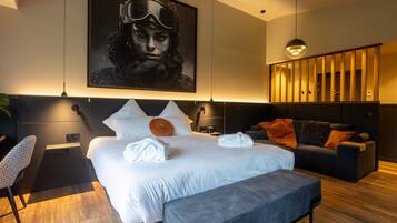 A modern hotel room with a large bed, a sofa, a desk, and a large framed picture on the wall.