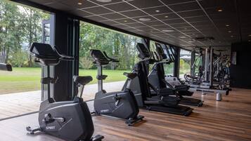 Un gimnasio con varias máquinas de cardio, ventanas amplias y suelo de madera.