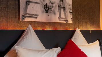Habitación de hotel con una cama, almohadas blancas y rojas, y una fotografía grande en blanco y negro en la pared.