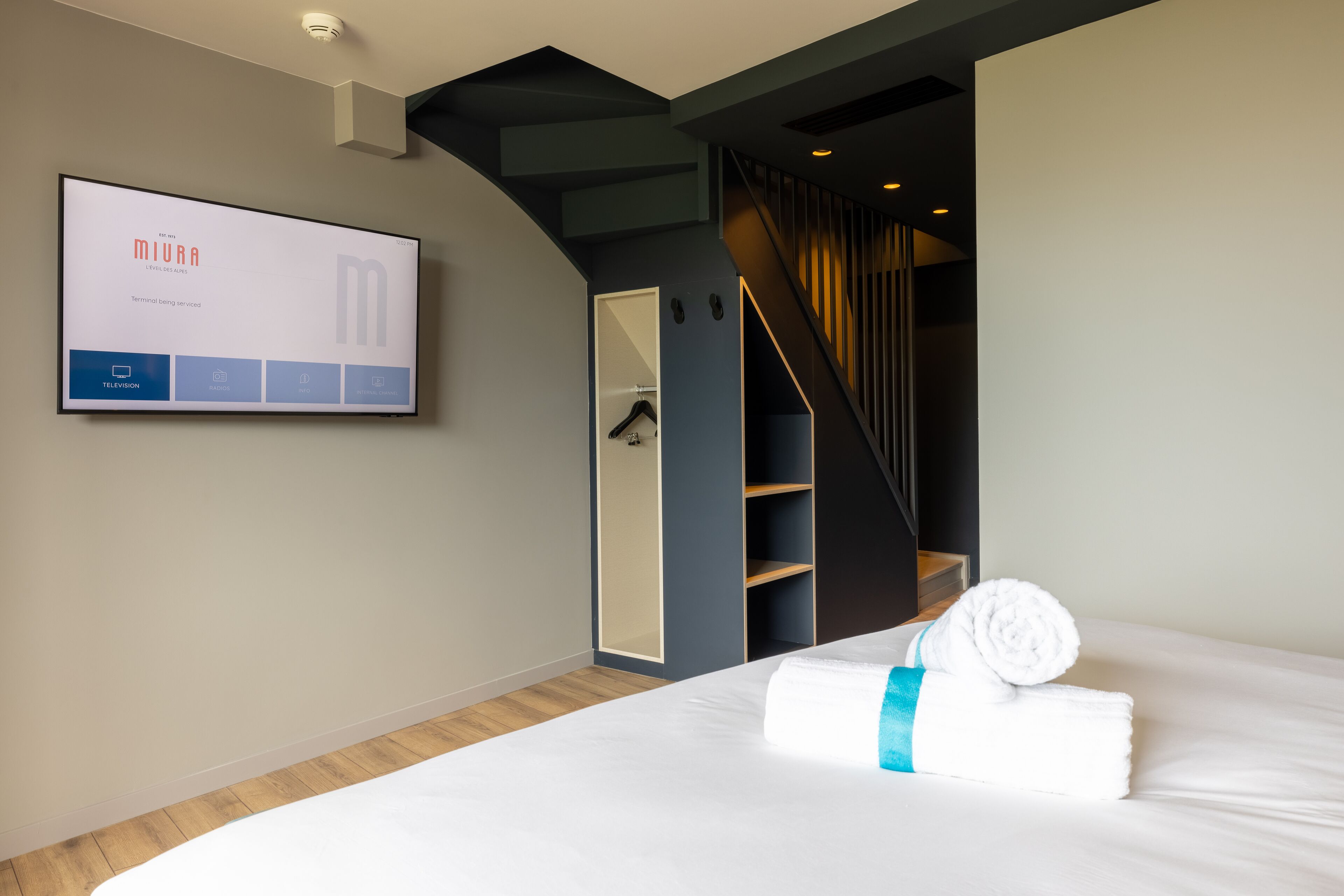 A hotel room with a bed, a TV mounted on the wall, a wardrobe, and a staircase.