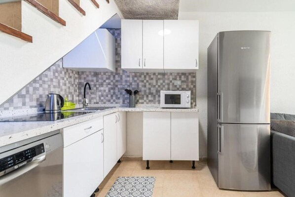 A compact kitchen with white cabinets, a stainless steel refrigerator, a microwave, and a kettle on the countertop.