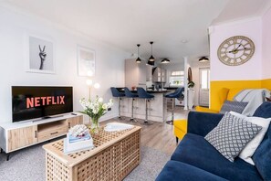 Relax in a spacious living area with a large flat-screen TV and comfortable sofa, plus a kitchen with a bar area and modern appliances.