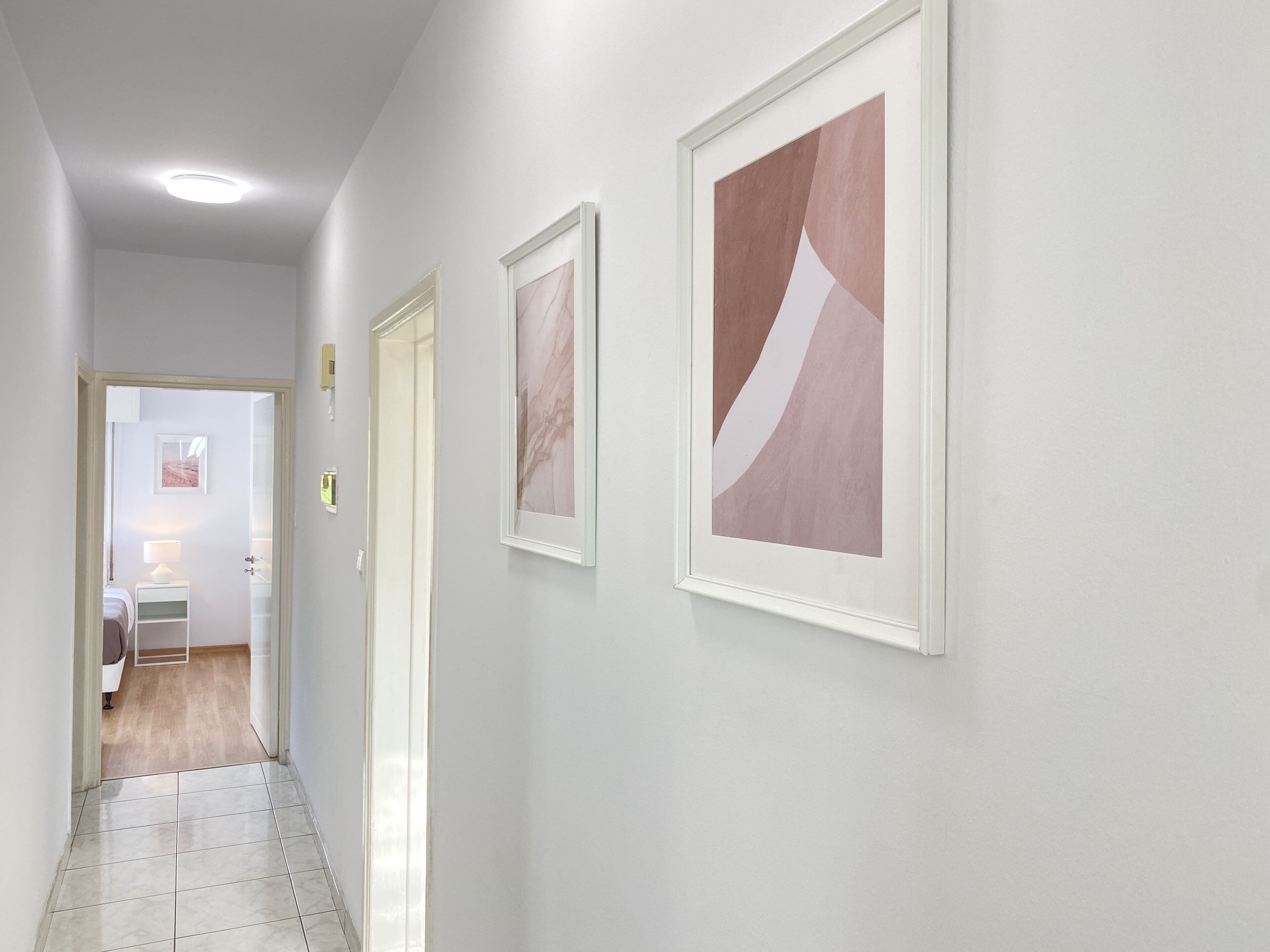 Un pasillo con suelo de baldosas, paredes blancas y cuadros abstractos.