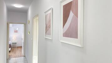 Un pasillo con suelo de baldosas, paredes blancas y cuadros abstractos.