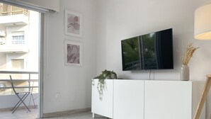 Un salon moderne avec un meuble blanc, un téléviseur à écran plat fixé au mur et une plante en pot posée sur le meuble.