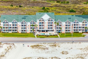 Un hotel frente a la playa con varios balcones, piscina y un césped verde.