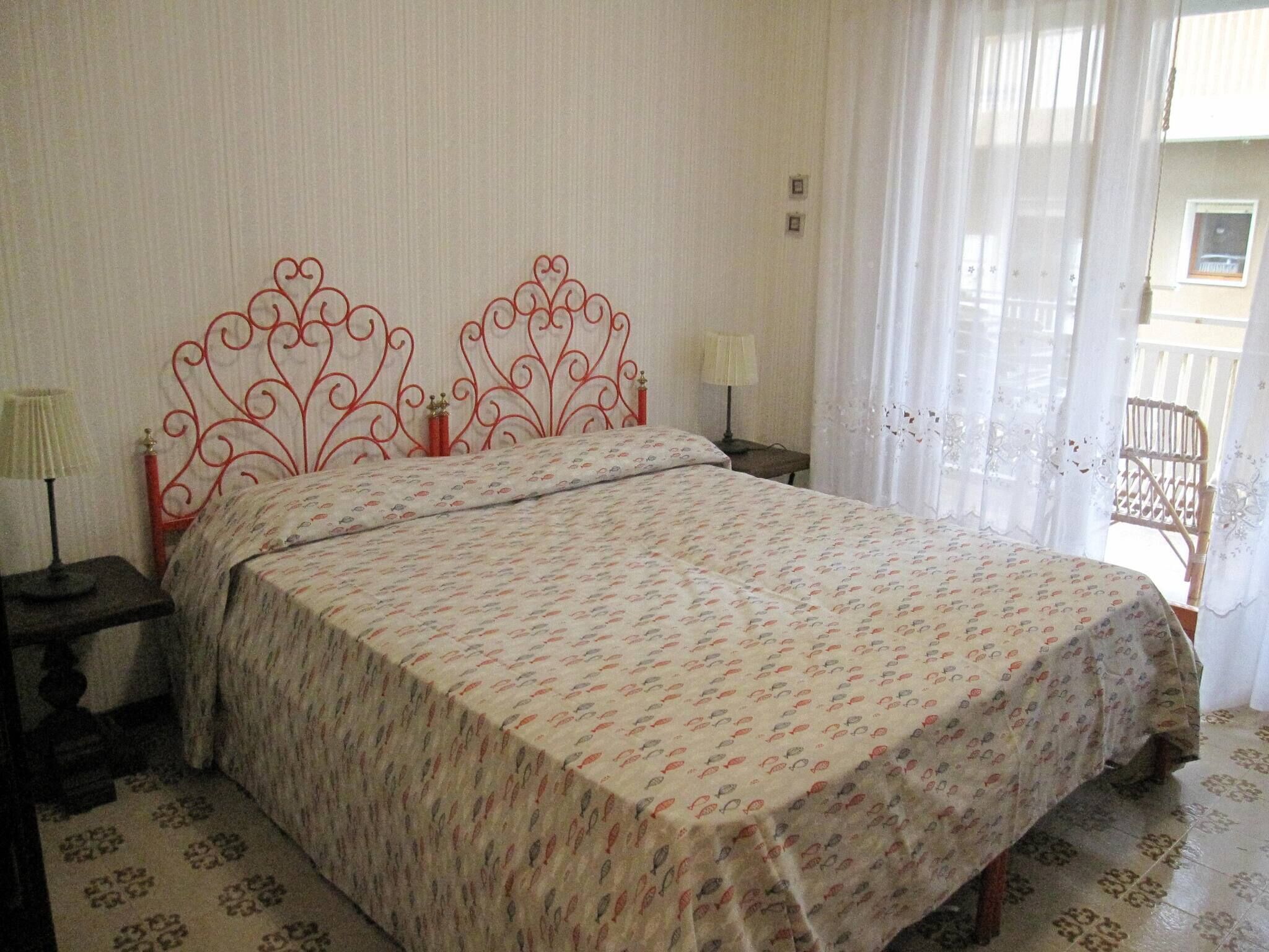 Une chambre à coucher avec un lit, deux lampes de chevet, une chaise et une fenêtre avec des rideaux.