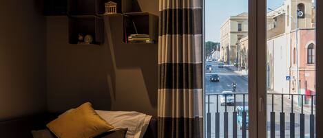A hotel room with a bed, a view of the street, and a balcony with a railing.