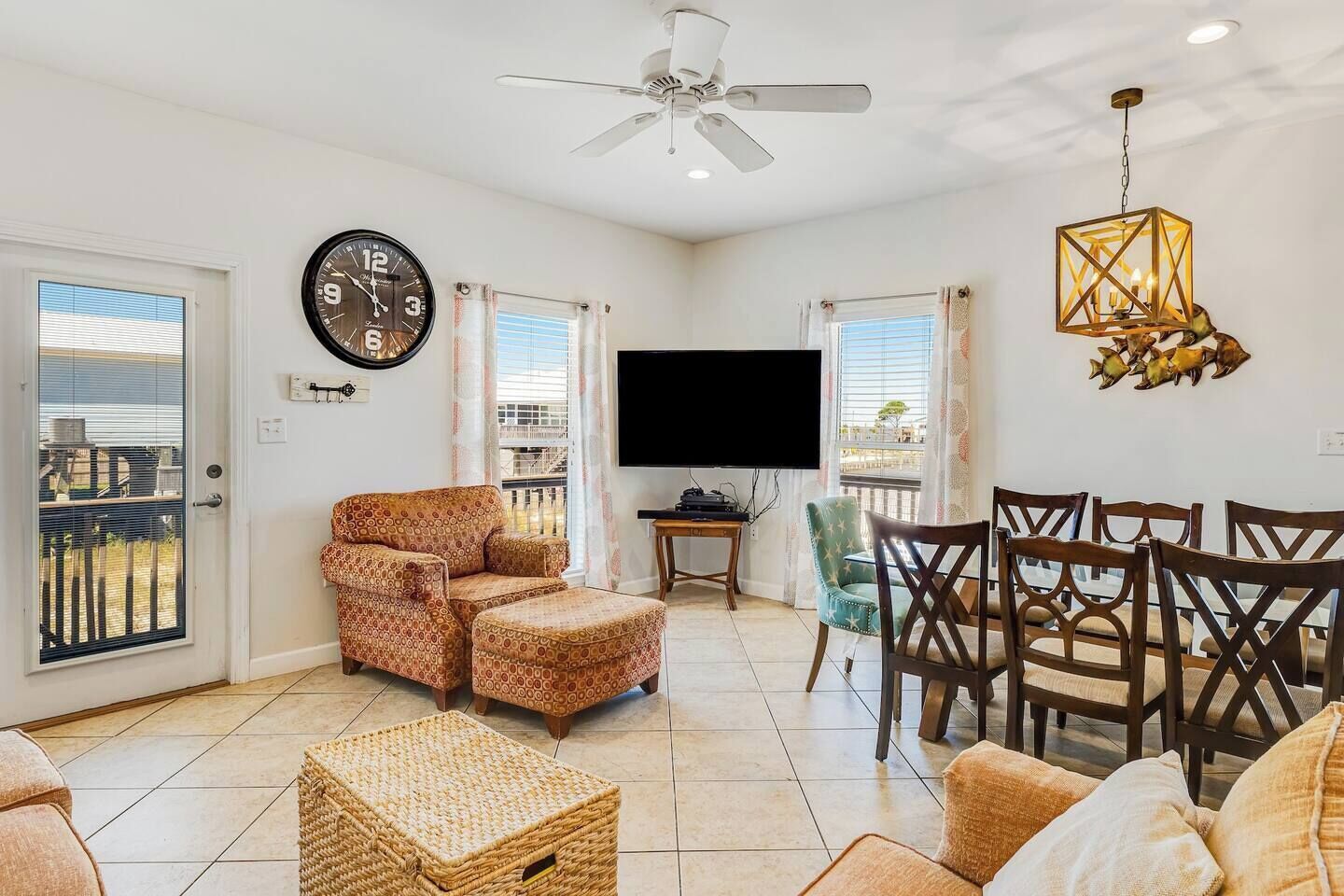 A living room with a ceiling fan, a TV, a clock, and a dining area with chairs and a table.