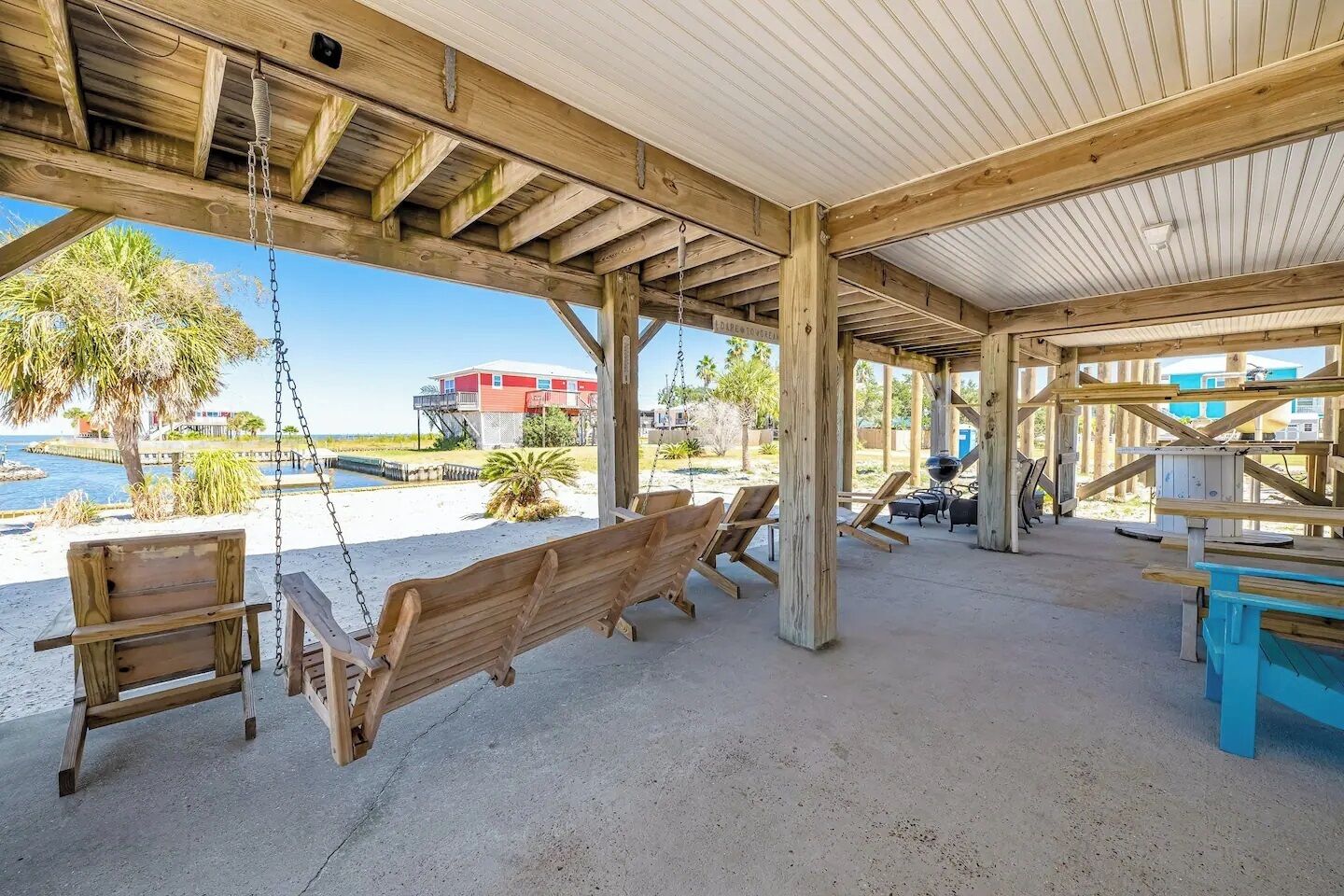 Un espacio al aire libre cubierto con bancos de madera y un columpio, con vistas a una playa y un edificio.