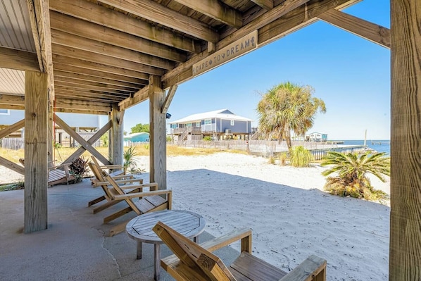 Un cabanon de plage en bois, équipé d’une table et de chaises, qui offre une vue sur une plage de sable et l’océan.