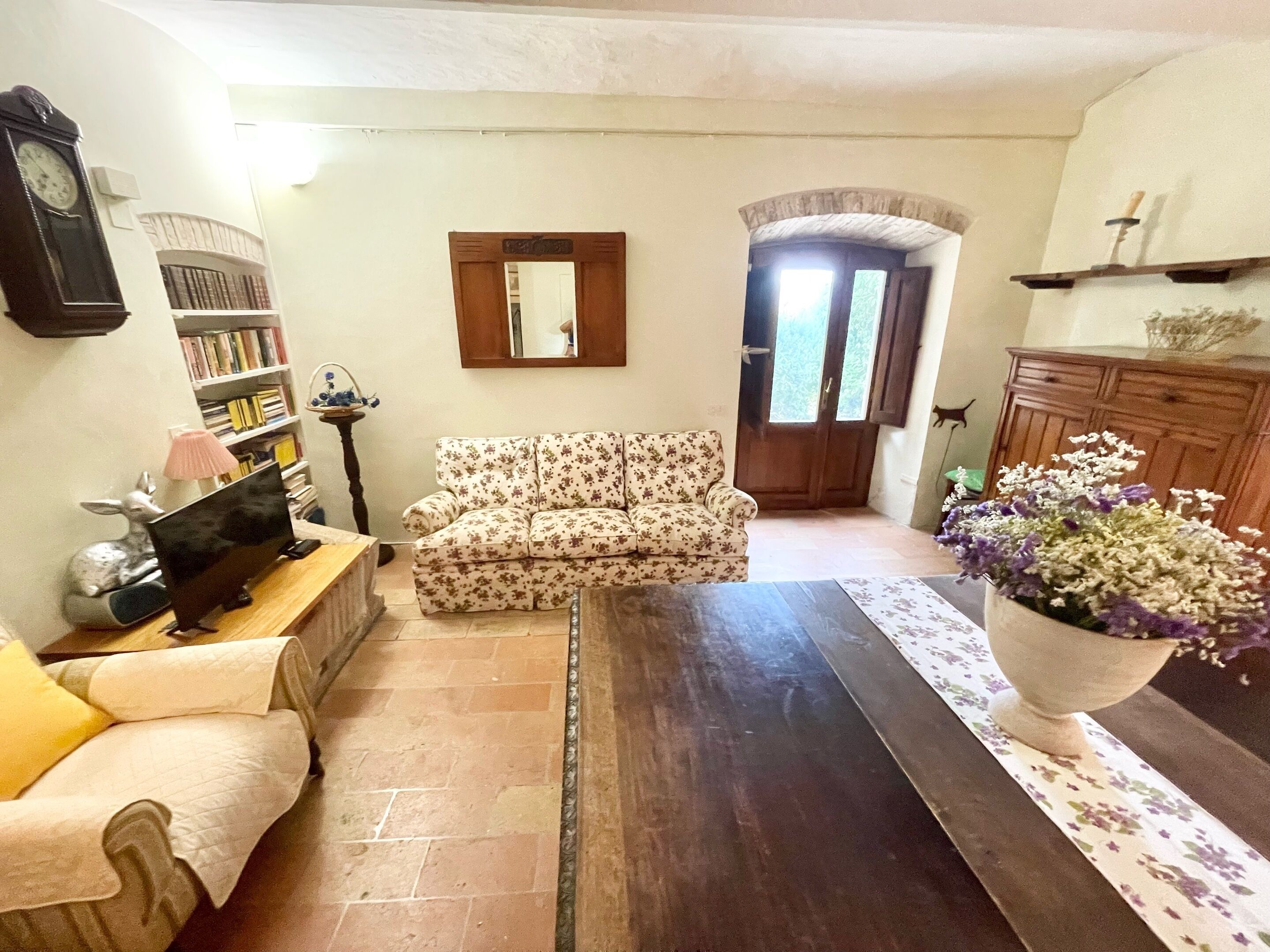 A living room with a sofa, a coffee table, a bookshelf, a clock, and a door leading outside.