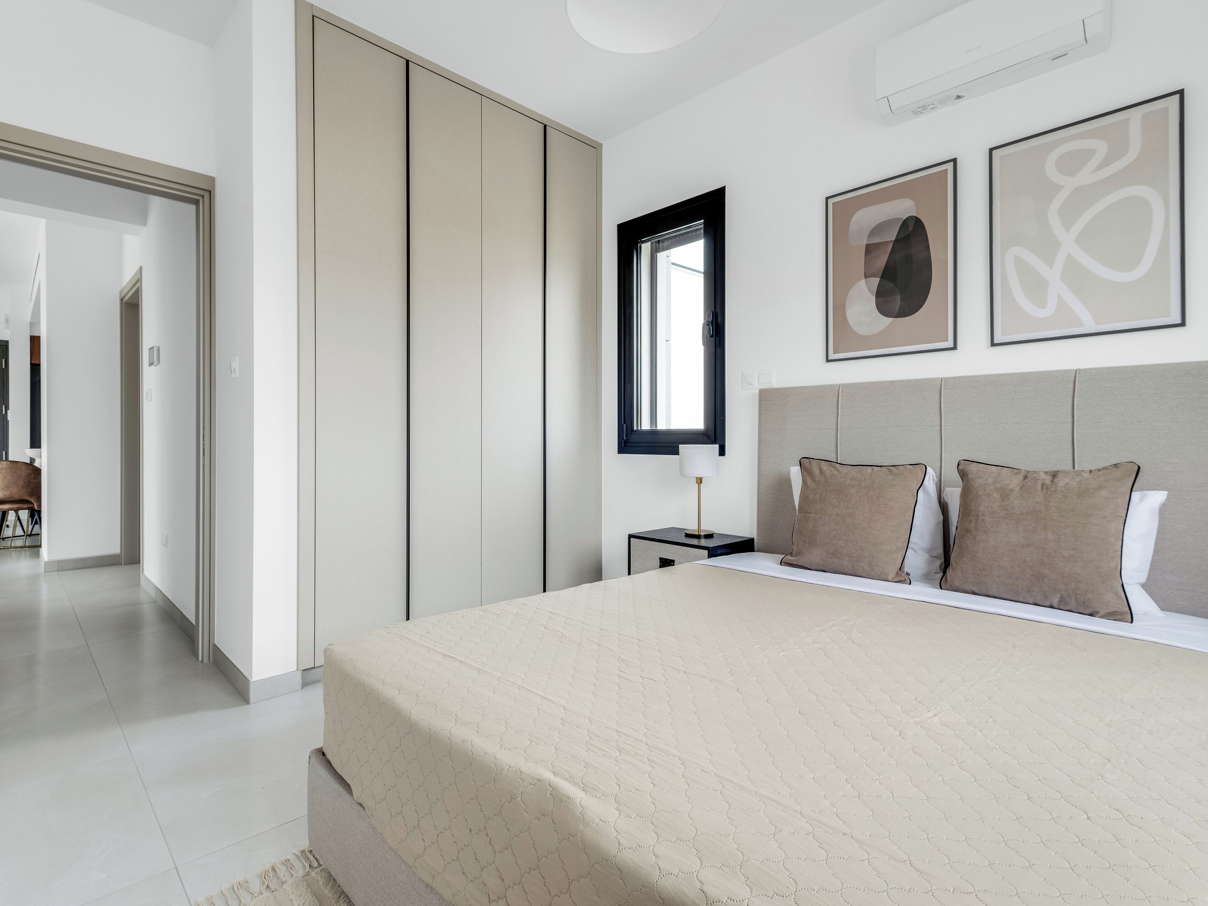 Un dormitorio moderno con una cama grande, una mesita de noche, un ventanal y dos cuadros abstractos en la pared.