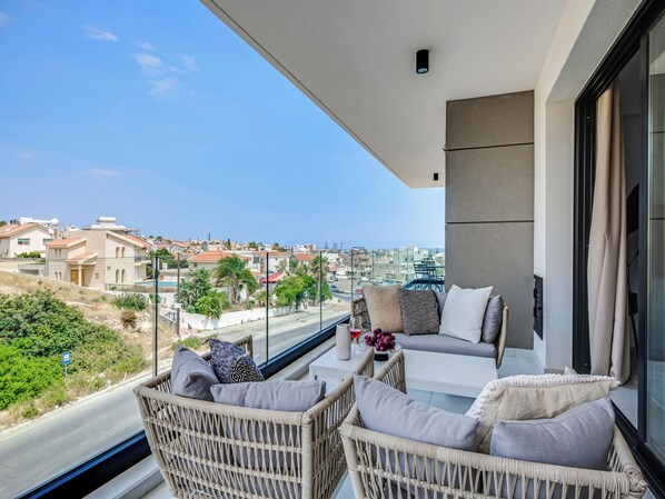 Ein Balkon mit Korbstühlen und Kissen, der auf einen Wohnbereich mit Häusern und einem klaren Himmel blickt.
